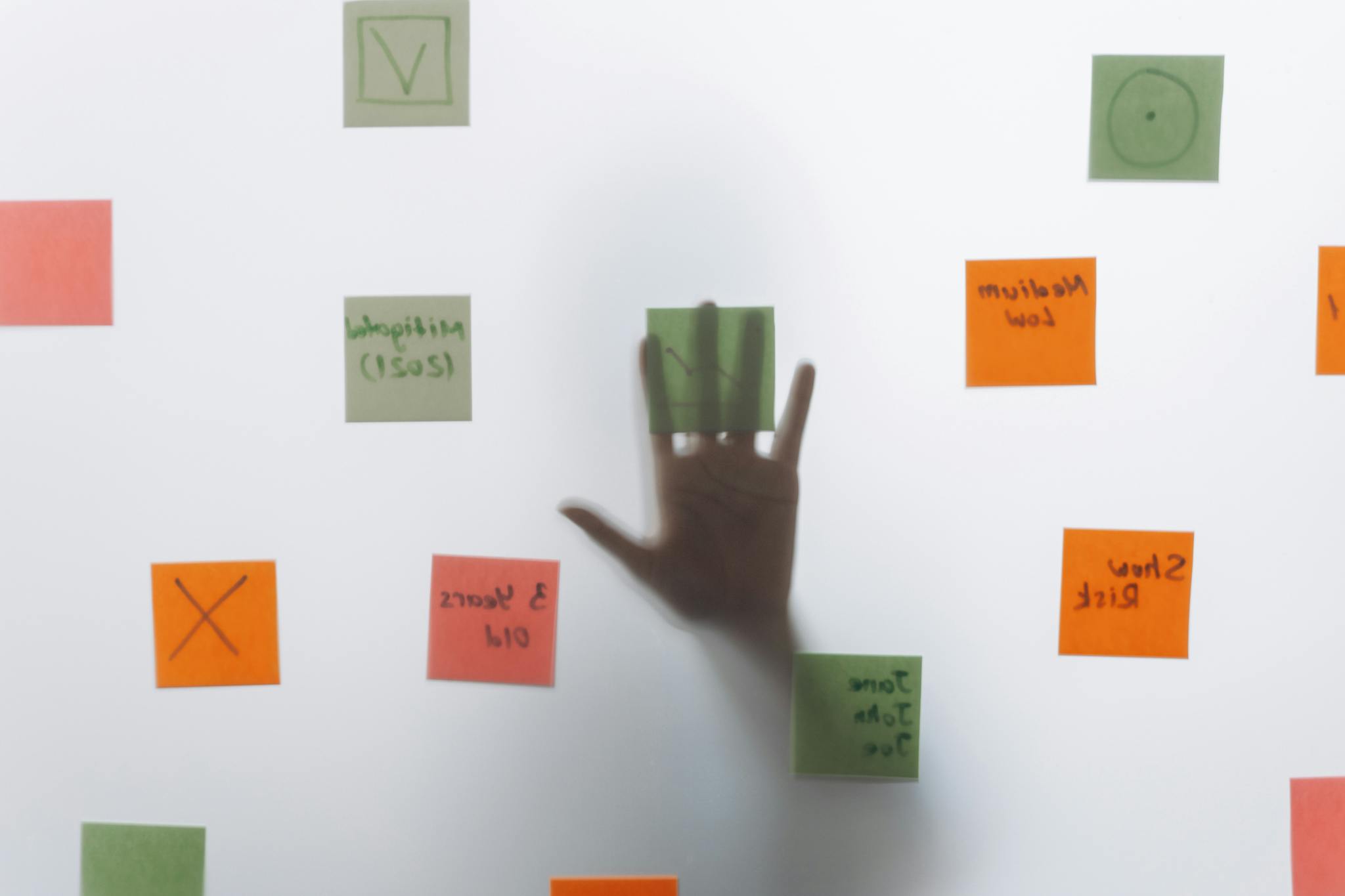 A hand reaching behind glass covered with colorful sticky notes, symbolizing brainstorming and ideas.